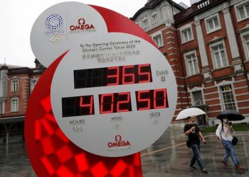 Passersby wearing protective face masks walk past a countdown clock for the Tokyo 2020 Olympic Games, on the day to mark the one-year countdown to the summer games that have been postponed to 2021 due to the coronavirus disease (COVID-19) outbreak, in Tokyo, Japan July 23, 2020.  REUTERS/Issei Kato