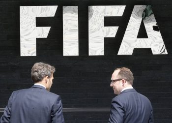 Two men talk to each other in front of the FIFA logo at the FIFA headquarters in Zurich, Switzerland, Wednesday, May 27, 2015. Swiss prosecutors opened criminal proceedings into FIFA's awarding of the 2018 and 2022 World Cups, only hours after seven soccer officials were arrested Wednesday pending extradition to the U.S. in a separate probe of "rampant, systemic, and deep-rooted" corruption. (AP Photo/Michael Probst)