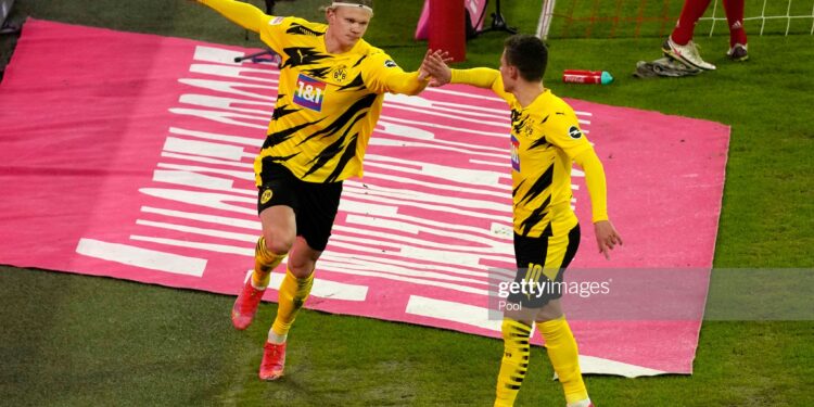 MUNICH, GERMANY - MARCH 06: Erling Haaland of Borussia Dortmund  celebrates with teammate Thorgan Hazard  after scoring their team's second goal  during the Bundesliga match between FC Bayern Muenchen and Borussia Dortmund at Allianz Arena on March 06, 2021 in Munich, Germany. Sporting stadiums around Germany remain under strict restrictions due to the Coronavirus Pandemic as Government social distancing laws prohibit fans inside venues resulting in games being played behind closed doors. (Photo by Günter Schiffmann - Pool/Getty Images)