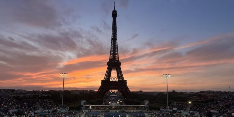 Spectators photograph a colorful sunset at Eiffel Tower Stadium prior to a beach volleyball match between The United States and Canada at the 2024 Summer Olympics, Saturday, July 27, 2024, in Paris, France. (Wally Skalij/Los Angeles Times)